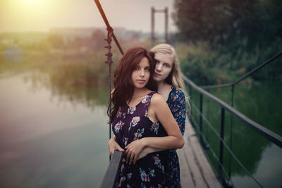 Lesbian couple embracing on footbridge against sky