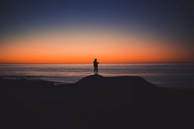 Silhouette man looking at sea against sky during sunset