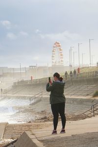 Rear view of woman photographing at beach against sky