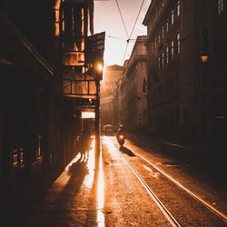 Illuminated street amidst buildings in city against sky