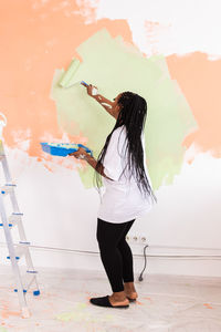 Rear view of woman with umbrella standing against wall