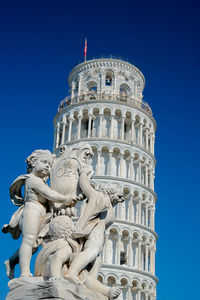 Low angle view of leaning tower of pisa and sculpture against blue sky