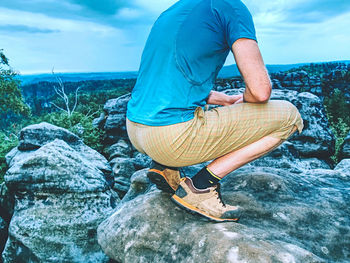 Rear view of man sitting on rock by sea against sky