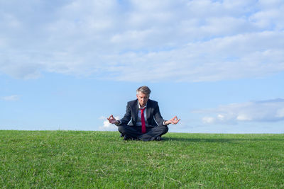 Man doing yoga on grassy field against sky