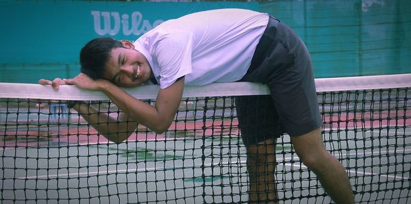 Male athlete leaning on tennis net on court