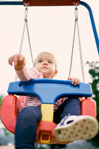 Low angle view of boy sitting on swing at playground