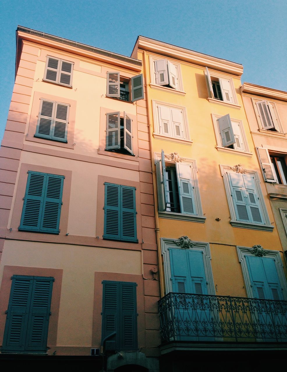 architecture, building exterior, built structure, low angle view, window, building, clear sky, residential building, residential structure, yellow, sky, day, outdoors, city, no people, facade, blue, balcony, sunlight, house