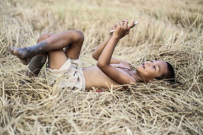 Boy using mobile phone while lying on field at farm