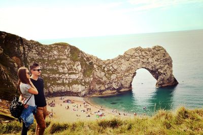 Friends standing on cliff by sea against sky