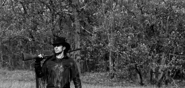 Man with rifle standing against trees