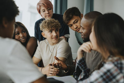 Teenage boys and girls with non-binary person listening to male teacher discussing in classroom