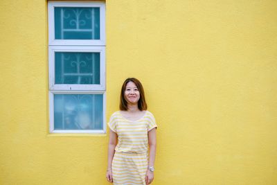 Portrait of smiling woman standing against yellow wall