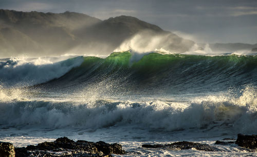 Waves splashing on rocks against sky during sunset