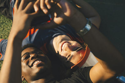 High angle view of smiling friends using smart phone while lying in park