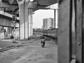 Rear view of man riding motorcycle by train under bridge