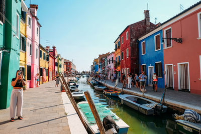 People on canal amidst buildings in city against sky