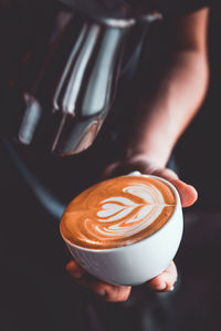 Midsection of barista pouring milk in coffee at cafe