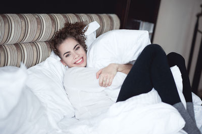 Smiling woman embracing with pillow lying on bed