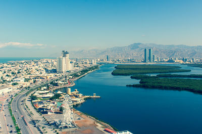 Aerial view of buildings by sea against blue sky