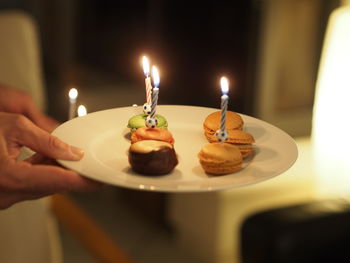 Cropped hand of woman holding lit candles on table