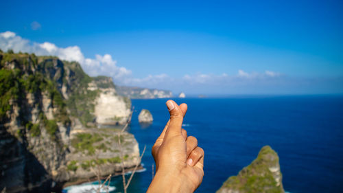 Midsection of person on rock by sea against blue sky