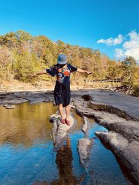 Full length of woman standing on rock in forest against sky