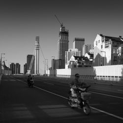 Vehicles on road by buildings against clear sky