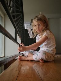 Girl holding railing while sitting on hardwood floor at home