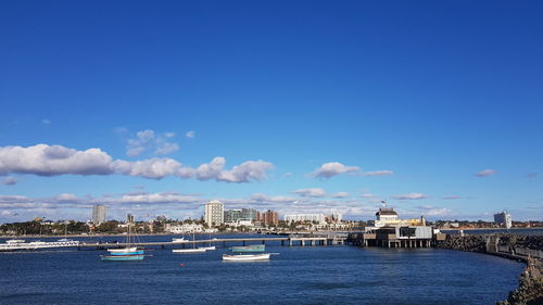 Sailboats in sea by buildings against blue sky