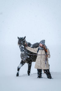 Woman with horse standing on snow covered land during winter