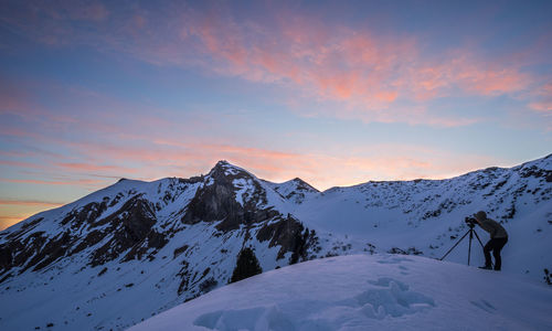 Man photographing on snowcapped mountain at sunset