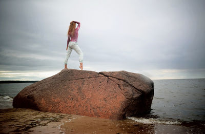 Man standing on rock by sea against sky
