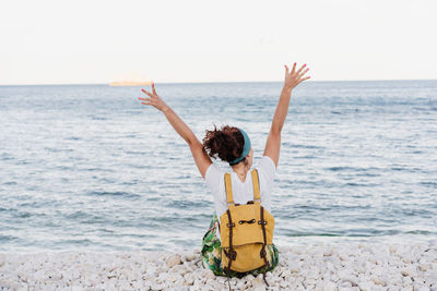 Rear view of person with arms raised on beach against sky