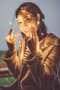 Portrait of woman holding illuminated string lights at night