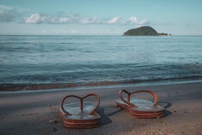 Scenic view of sea with flip-flops at beach against sky