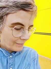 Close-up of smiling mature woman wearing eyeglasses by yellow wall