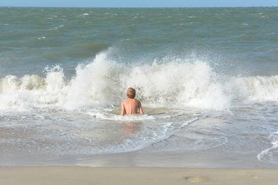 A boy sits in the water in a wave, on the sandy beach on the north sea coast in the netherlands,
