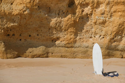 White surfboard in front of rock formation on beach