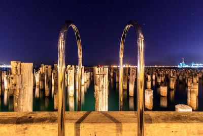 Wooden posts in sea against sky at night