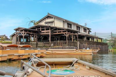 Fishing boats moored at harbor by building against sky