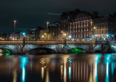 Illuminated bridge over river in city at night