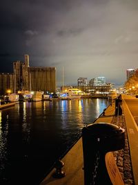 Illuminated city by river against sky at night