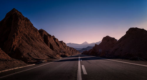 Road leading towards mountains against clear sky