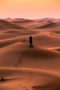 Mid distance view of silhouette man standing at desert during sunset