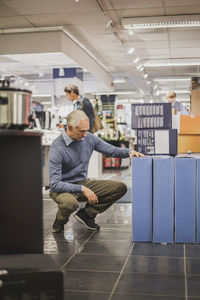 Mature owner looking at products while crouching in electronics store