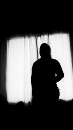 Rear view of silhouette man sitting against window at home