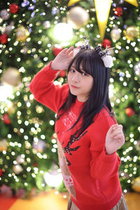 Portrait of young woman standing by christmas tree at night