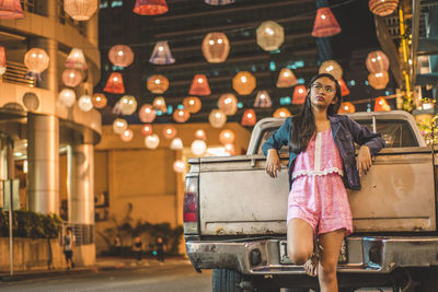 Teenage girl leaning on pick-up truck at illuminated street