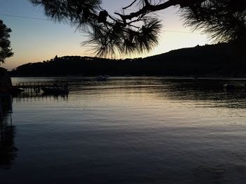 Silhouette palm trees by lake against sky at sunset