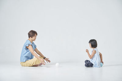 Side view of mother and daughter sitting on gray background